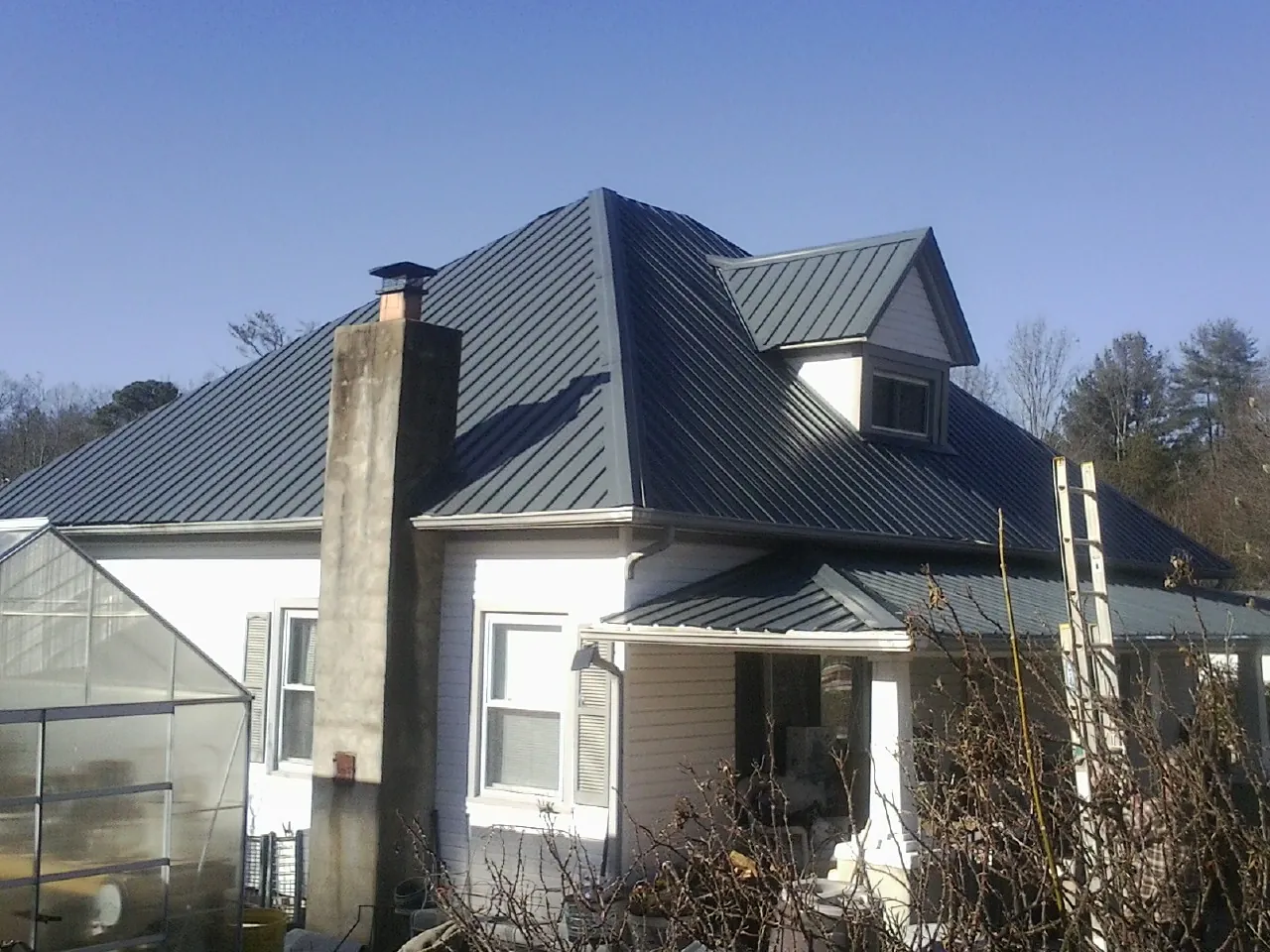 Dark blue standing seam metal roof on a white farmhouse with dormer — Slate & Tile Roof Repair by Roofing Brothers in Rocky Point
