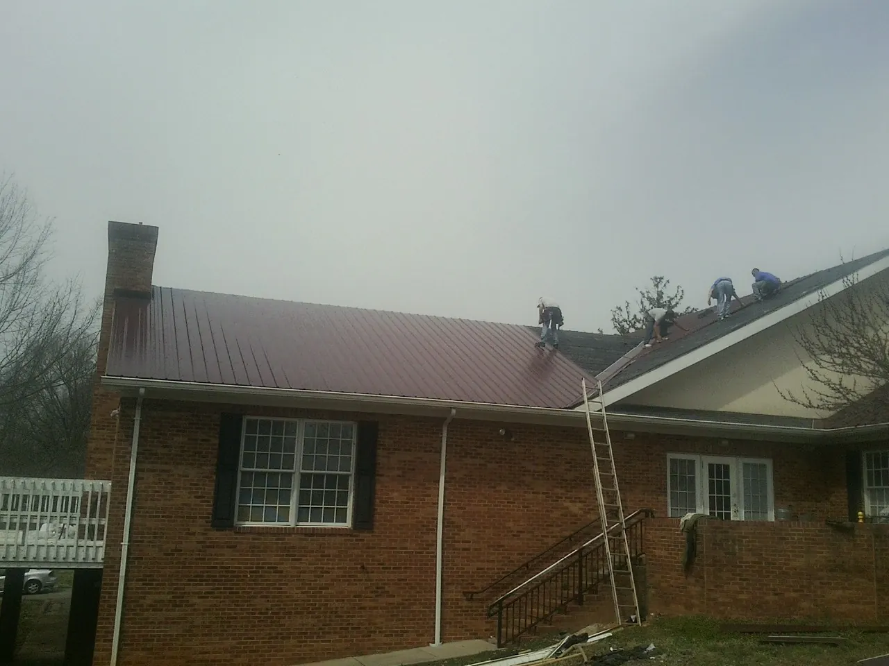 Crew setting red metal roofing panels on a brick home in Rocky Point