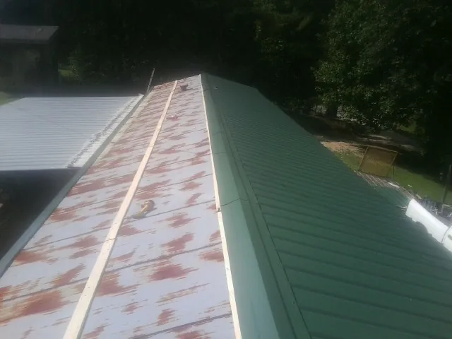 Old rusted panels beside newly installed green metal roofing — Wind Damage Roof Repair by Roofing Brothers in Rocky Point