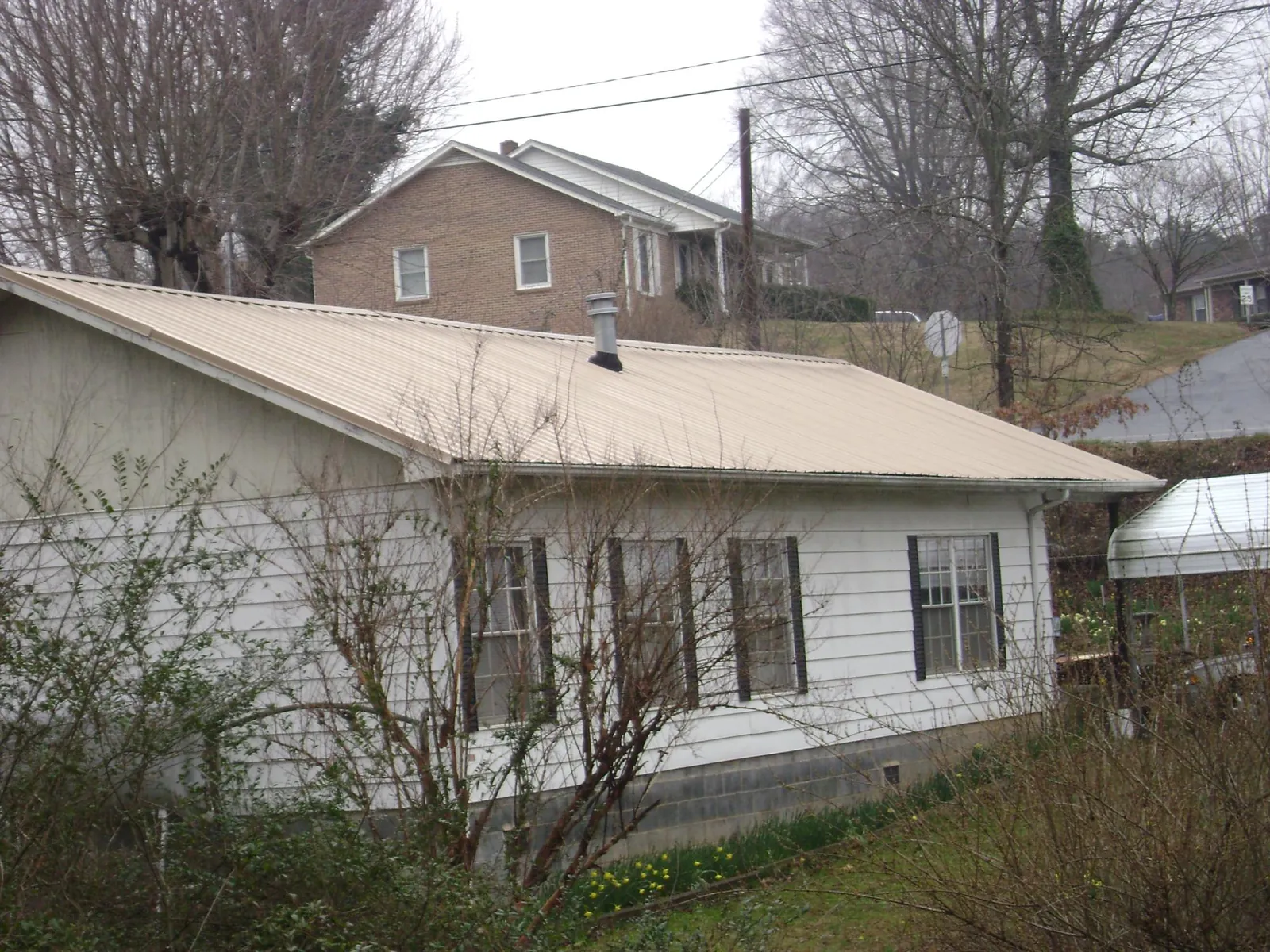 Tan metal roof on a white sided house set into a hillside — Commercial Roofing by Roofing Brothers in Rocky Point