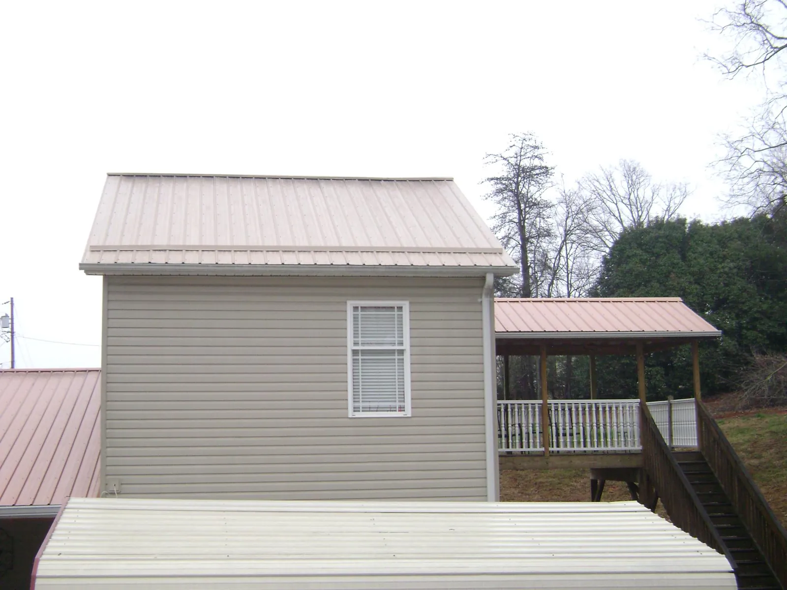 Tan metal roofs on a two story addition and attached porch, from a Roof Replacement job in Rocky Point